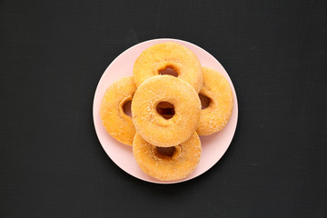 Homemade autumn apple-cinnamon donuts on a pink plate on a black surface, top view. Flat lay, overhead, from above.