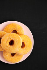 Homemade autumn apple-cinnamon donuts on a pink plate on a black surface, top view. Flat lay, overhead, from above.