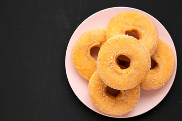 Overhead view, homemade autumn apple-cinnamon donuts on a pink plate on a black surface. Flat lay, overhead, top view. Copy space.