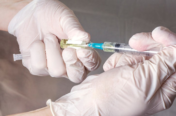 Gloved hands type the yellow vaccine into the syringe. The concept of vaccination