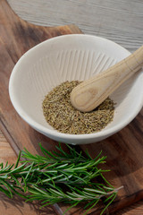 Ground rosemary and leaves with a pestle and mortar on a wooden chopping board