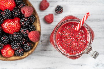 Fresh organic red smoothie in glass mug on white table, close up, top view. Refreshing summer fruit drink. Blackberry, raspberry and strawberry smoothie