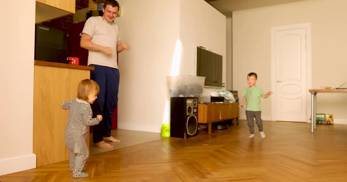 Careful cheerful father having fun and dancing with active cute children at spacious living room at home