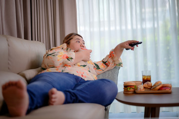 plump woman holding remote control while eating junk food, stay in living room enjot eating whole...