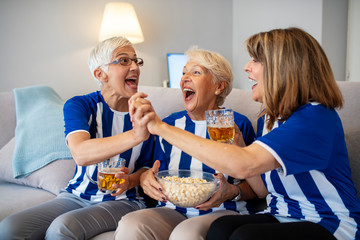 Elderly Woman Fans Emotionally Watching Soccer on Tv. Senior women watching football on TV. Cheerful fans in Sports Jersey. Female friends watching football game.