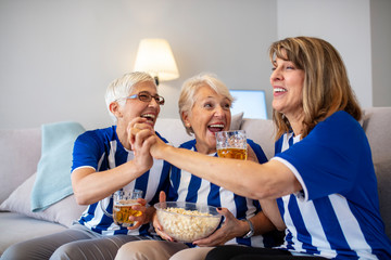 Football fans watching a game on tv. Sports fans rooting for their team. Elderly Woman Fans Emotionally Watching Soccer on Tv  and celebrating victory at home. Excited senior women watching a game