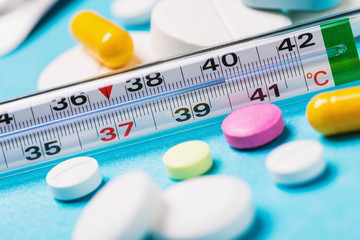 Thermometer with a temperature of 40 degrees with various tablets on a blue background. The concept...