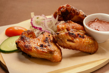 Fried chicken wings with onion rings and red sauce on a wooden board.