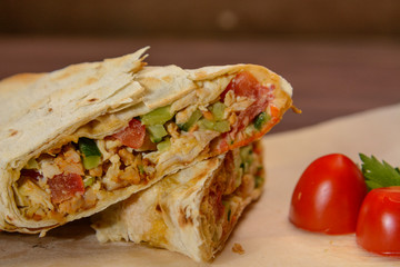 Sliced Shawarma with slices of tomato and herbs on the wood. Close up.