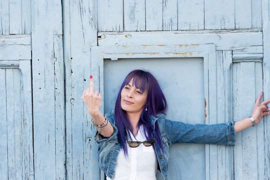 Mujer bella mostrando el dedo medio como insulto obsceno y ofensivo., con fondo de puerta vieja azul