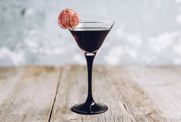 Martini cocktail with black vodka and figs on the rustic background. Selective focus. Shallow depth of field.