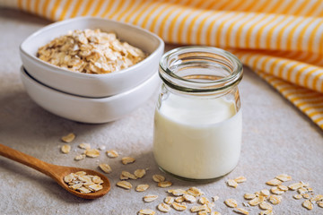 Bottle of oat milk and oat grains in bowl on table .