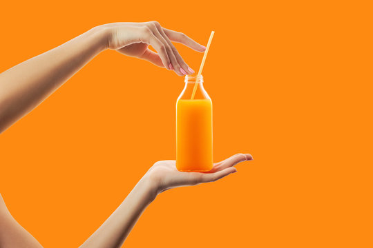 Female hands holding bottle with straw of fresh detox orange juice