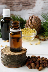 composition of cedar oil with pine nuts on a background of a branch with a pine cone, on a light wooden background
