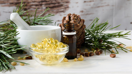 composition of cedar oil with pine nuts on a background of a branch with a pine cone, on a light wooden background