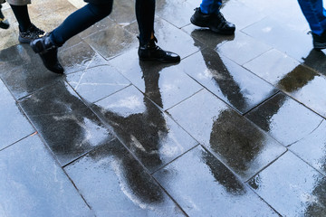Blurry reflection legs and shadows, silhouettes of the people in the wet sidewalk, in a puddle of...