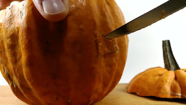 Carving pumpkin part 9, Person carving left eye into Halloween pumpkin with a small pointy serrated knife on wooden chopping board, STILL, ISOLATED