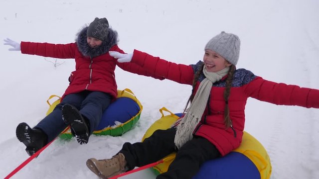 Happy children sledding in snow in winter and waving their hands. family plays in winter park during the Christmas holidays. children laugh and rejoice. Slow motion. concept of a happy family.