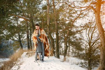 Fototapeta na wymiar happy couple wrapped in a blanket standing in the park on a snowy day