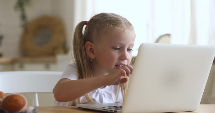 Curious cute little kid girl using laptop alone at home