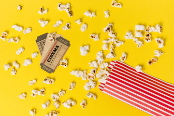 Cinema tickets over the spilled popcorns against yellow backdrop