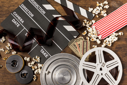Negatives stripes with clapperboard; film reels; tickets and popcorn on wooden desk