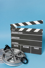 Obraz premium Clapperboard with film reel and film stripes against blue backdrop