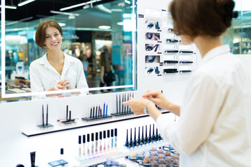 Young smiling woman in cosmetics shop is testing cosmetics in front of mirror