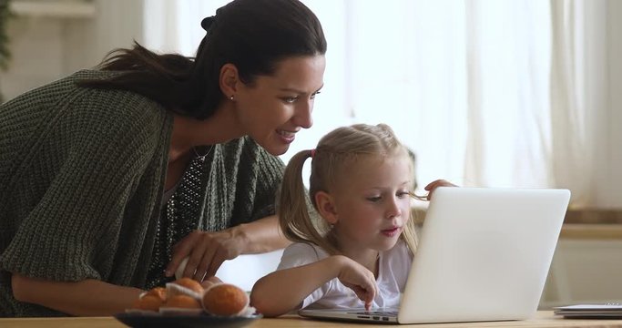 Kid girl using laptop with mom control at kitchen table