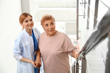 Nurse assisting elderly woman on stairs indoors