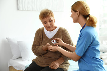 Nurse giving pills to elderly woman indoors. Medical assistance