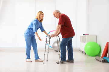 Caretaker helping elderly man with walking frame indoors