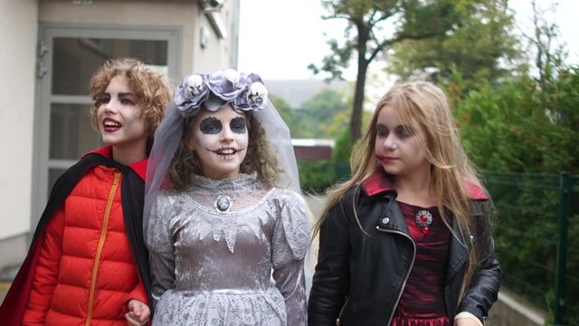 Happy Halloween walk. Children in costumes of a witch, a dead bride and a vampire walk along the street