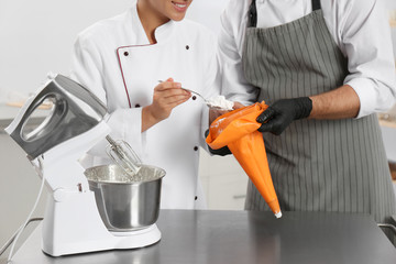 Pastry chefs preparing cream at table in kitchen, closeup
