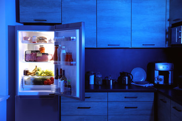 Open refrigerator full of products in kitchen at night