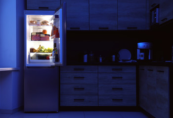 Open refrigerator full of products in kitchen at night