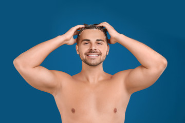 Fototapeta premium Young man washing hair on blue background