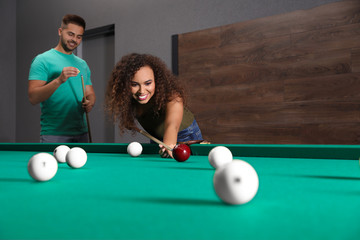 Young man and woman playing billiard indoors