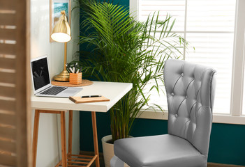 Stylish home workplace with elegant grey chair near window. Interior design