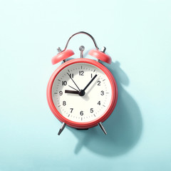 Red alarm clock with shadow lying on blue background. View from above.