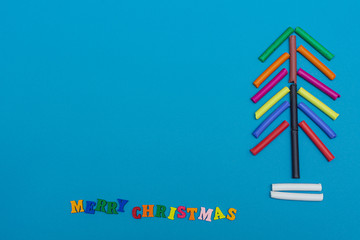 Christmas tree, composed of crayons pastel colors on a blue background.  Space for text, mock up, flat lay