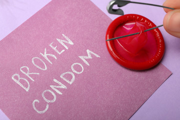 Woman piercing condom with pin on violet background, closeup. Safe sex
