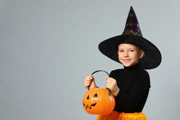 Cute little girl with pumpkin candy bucket wearing Halloween costume on grey background, space for text