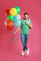 Young man jumping with bunch of colorful balloons on pink background