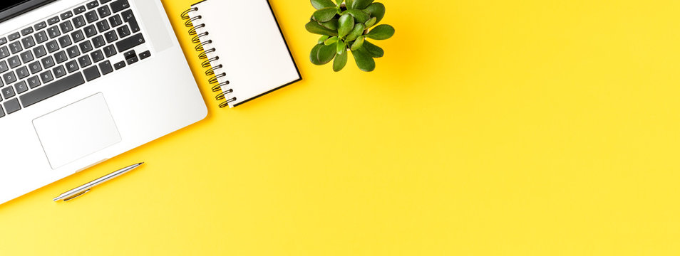 Office desktop with laptop, mobile phone, notebook and pen on yellow background with copyspace. Modern workplace. Banner
