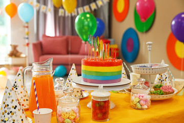 Bright birthday cake and other treats on table in decorated room