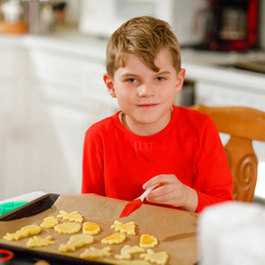 Cute little boy baking gingerbread Christmas cookies at home. Adorable blond child having fun in domestic kitchen. Traditional leisure with kids on Xmas.