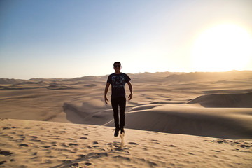 Fototapeta na wymiar young man on sand in a desert near Huacachina, Ica region, Peru. The sunset desert view