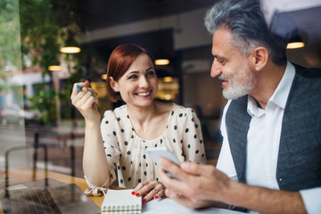 Man and woman having business meeting in a cafe, using smartphone.