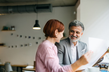 Man and woman having business meeting in a cafe, looking at blueprints.